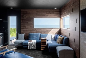 Una sala de estar moderna con un amplio ventanal con vistas al mar, una cocina integrada y un rincón de estar acogedor.