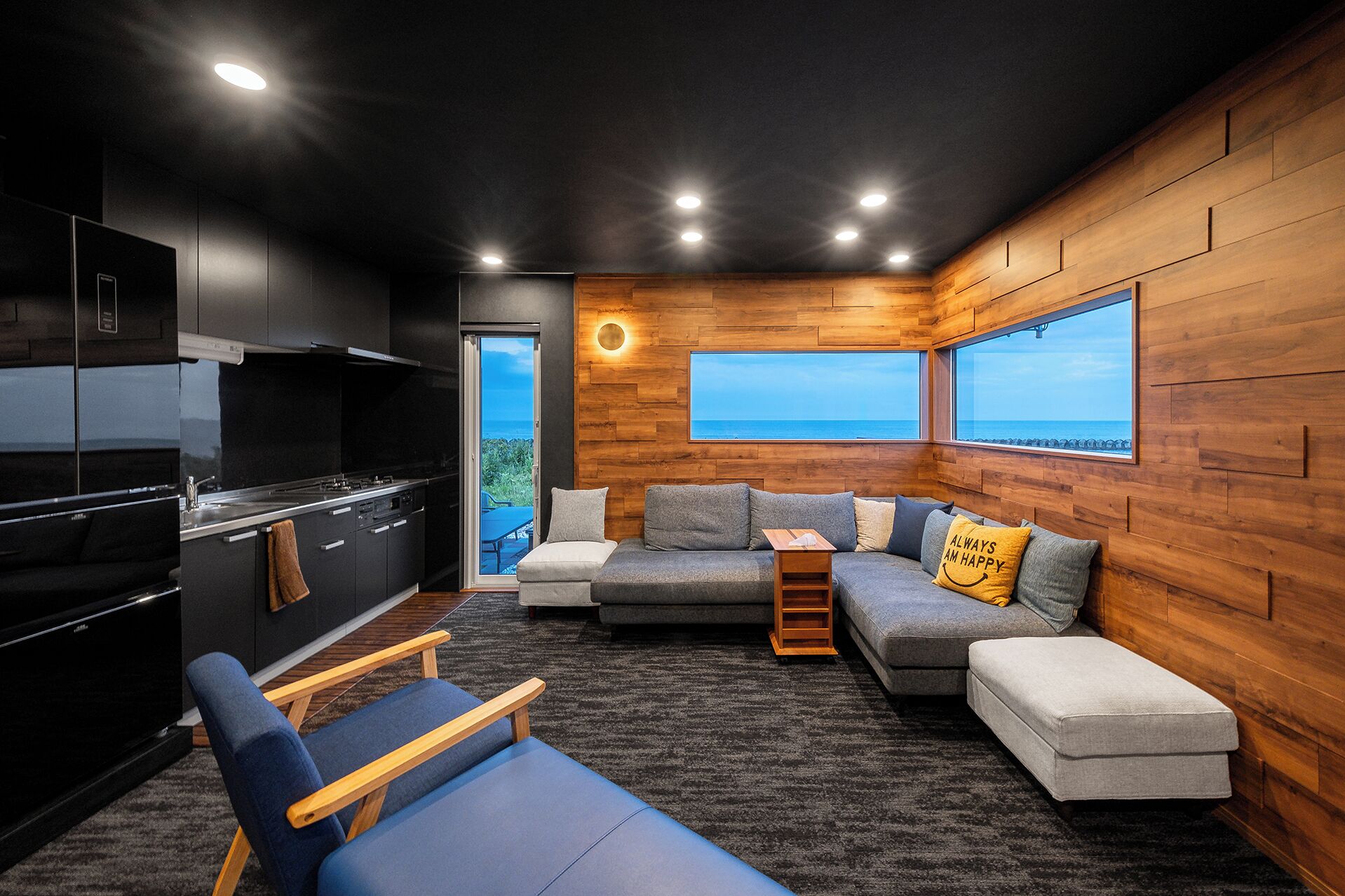 A compact living space with a kitchenette, a sofa set, and a view of the sea.