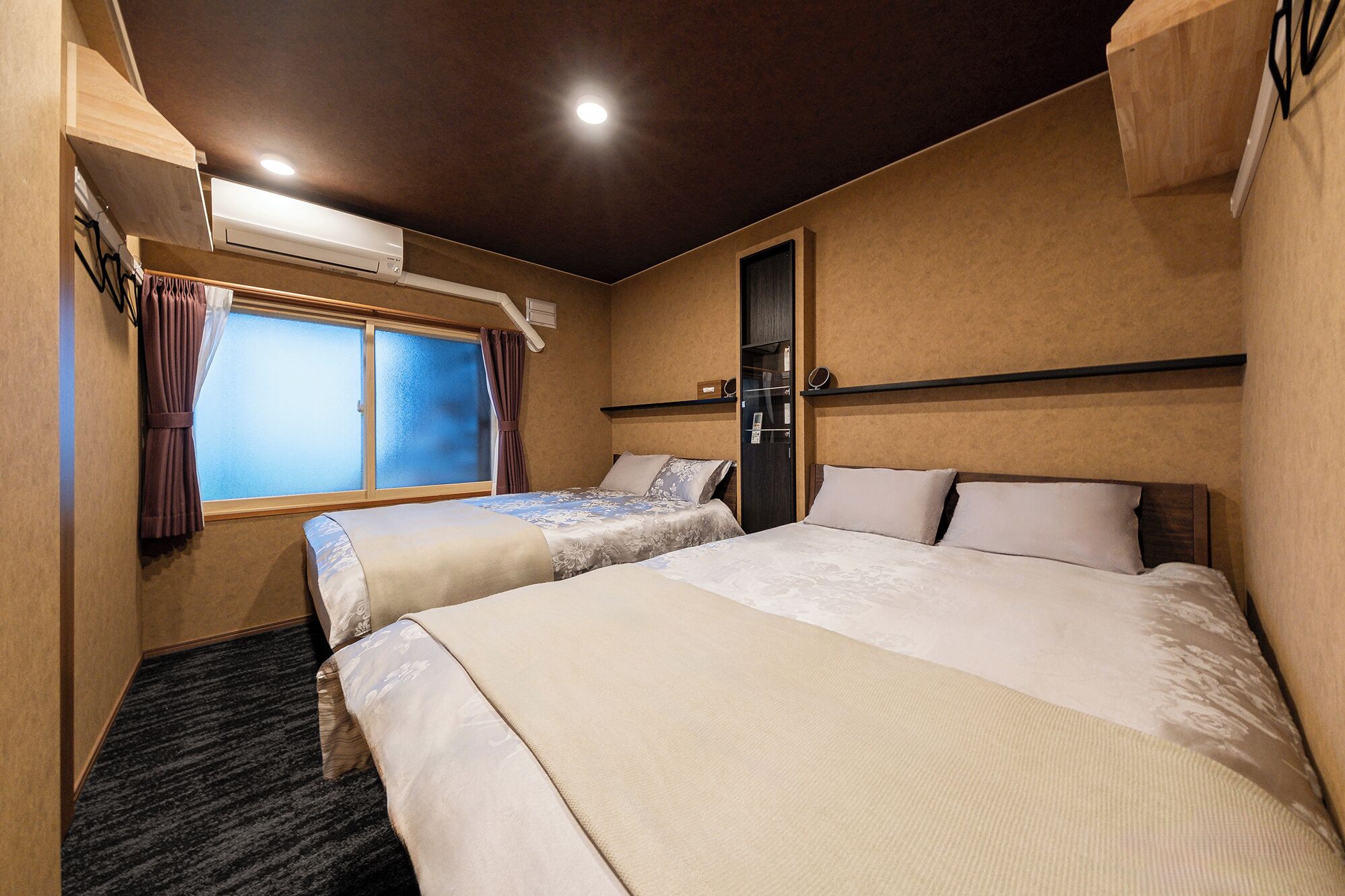 A hotel room with two beds, a window with curtains, an air conditioning unit, and a wooden headboard.