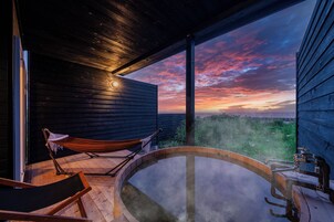 Un jacuzzi con vistas a un atardecer, una hamaca y una terraza de madera.