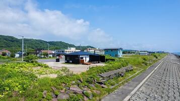 A coastal area with a paved walkway, a small building with a blue roof, and a hillside in the background.
