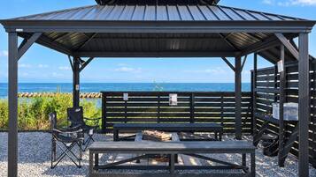 A covered outdoor seating area with a bench and a grill, overlooking a beach.