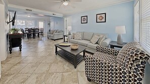 A living room with a sofa, a patterned armchair, a coffee table, and a dining area with chairs and a table.