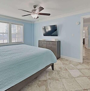 A bedroom with a bed, a ceiling fan, a TV, a dresser, and a window.