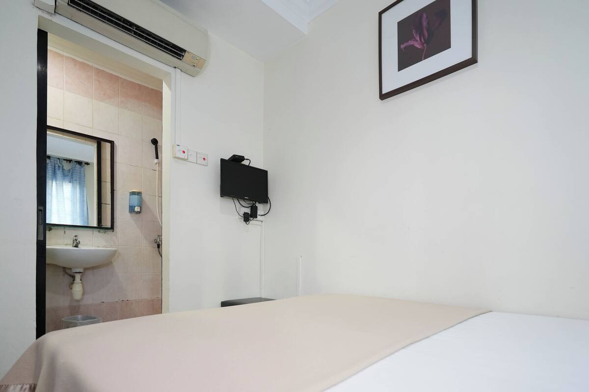 A hotel room with a bed, a sink, a mirror, and a TV mounted on the wall.