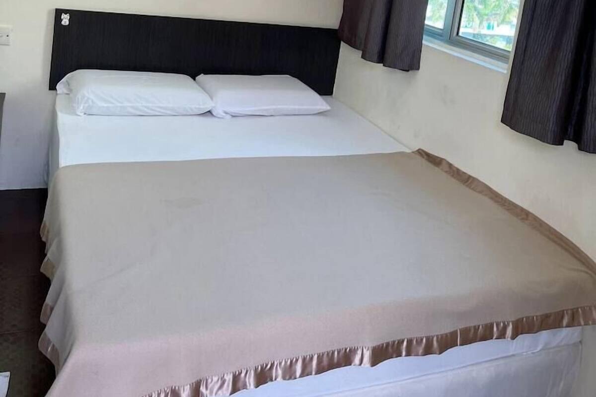 A hotel room with a bed, a framed picture on the wall, and a window with curtains.