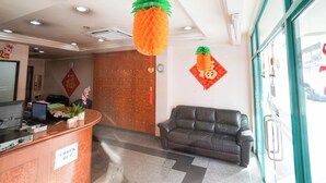 Zona de recepción con mostrador de salida, un sofá, una decoración de piña y un tapiz de pared con un carácter chino rojo.