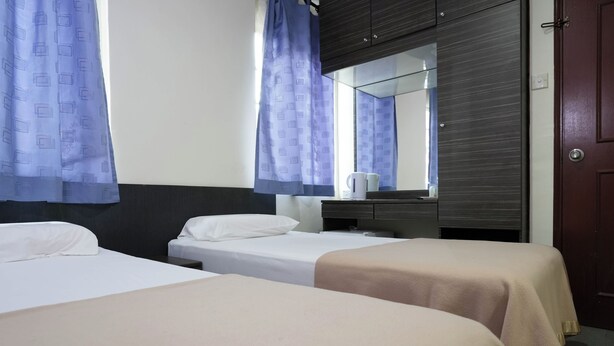 Habitación de hotel con dos camas individuales, un armario de madera, un espejo y una ventana con cortinas.