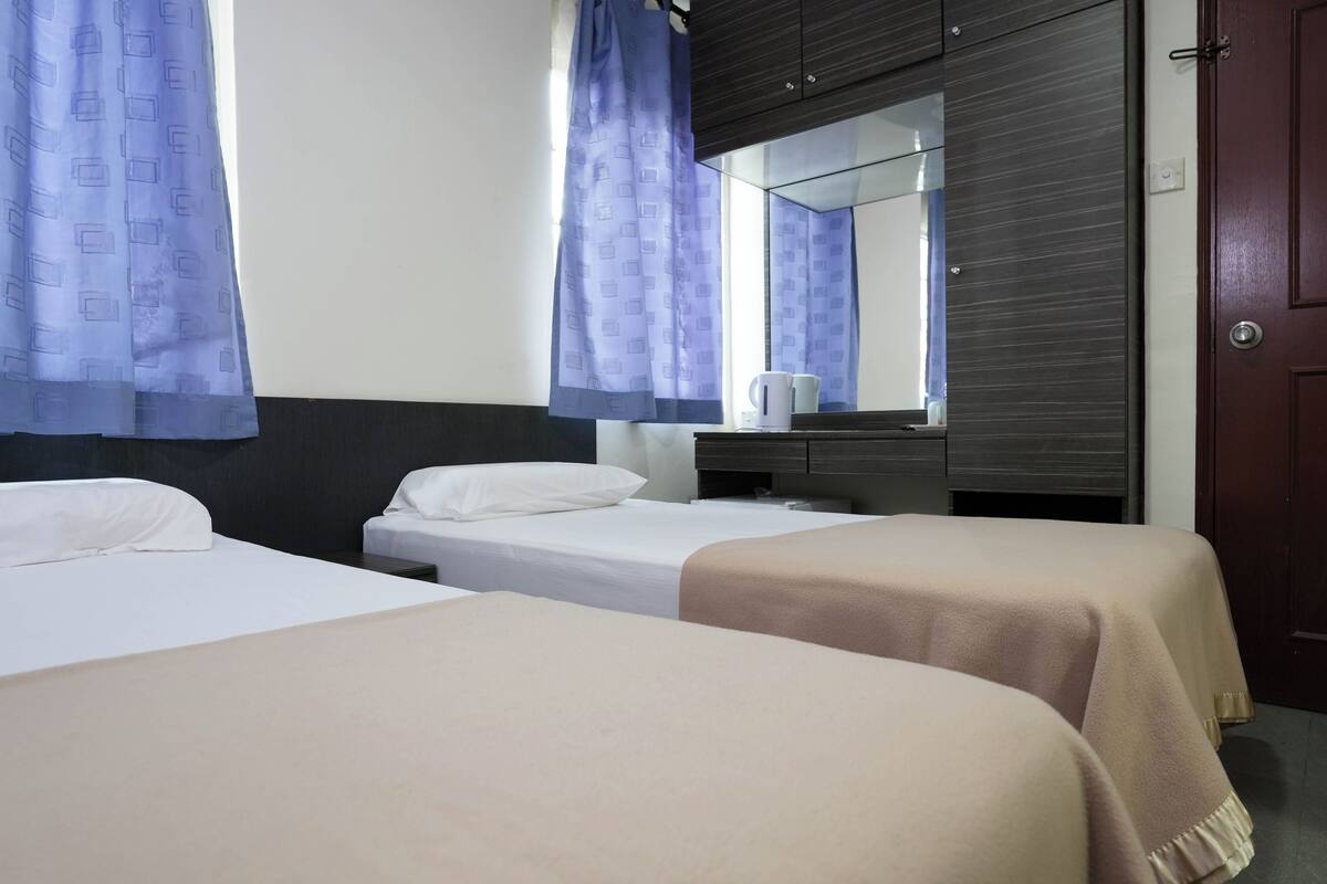A hotel room with two single beds, a wooden wardrobe, a mirror, and a window with curtains.