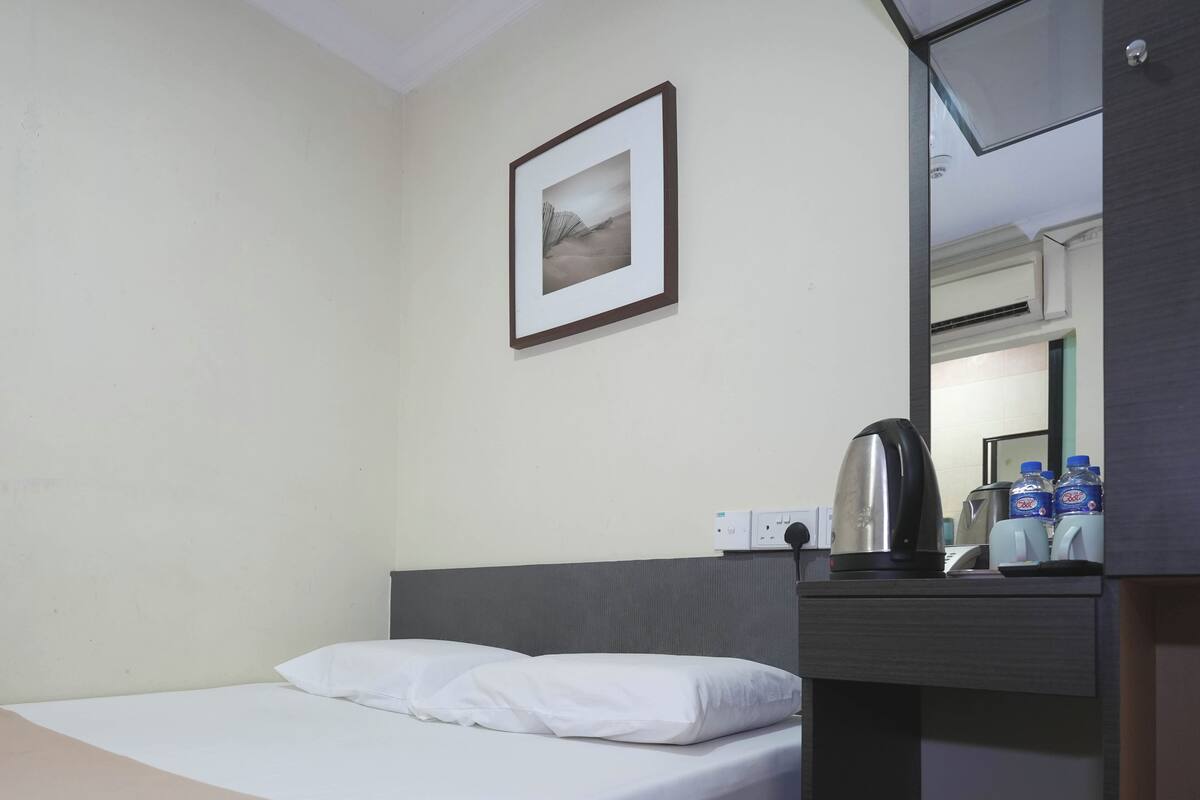 A hotel room with a bed, a framed picture on the wall, a kettle, and bottled water on the counter.