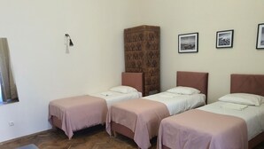 Ein Zimmer mit drei Einzelbetten, einem Holzboden im Fischgrätmuster, einem hohen Schrank und gerahmten Bildern an der Wand.