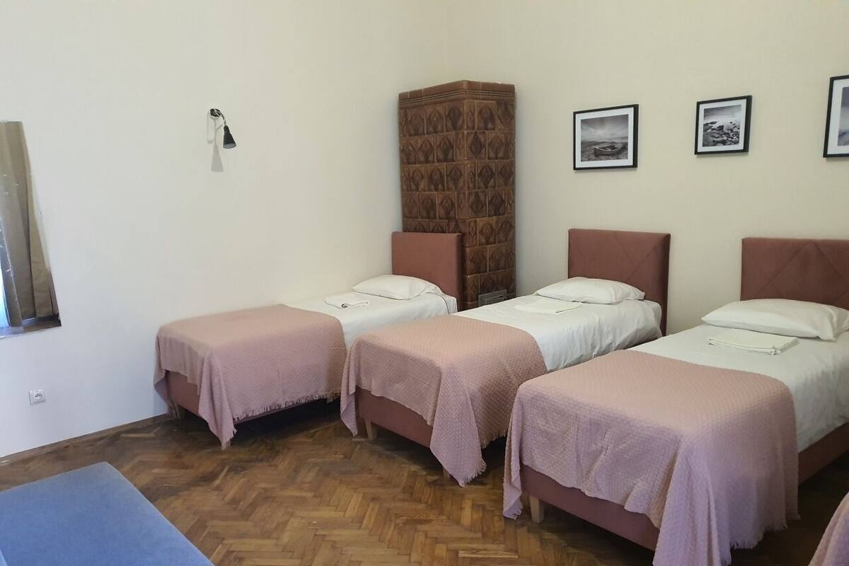 A room with three single beds, a wooden herringbone floor, a tall cabinet, and framed pictures on the wall.