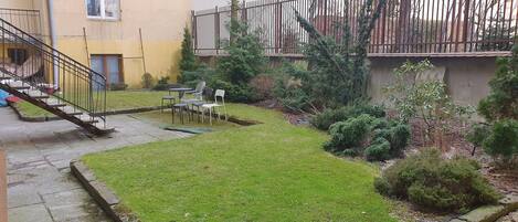 Um pátio com gramado, algumas cadeiras e uma escadaria que dá acesso a um andar superior.