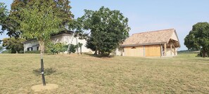 Uma propriedade rural com uma grande área gramada aberta, um edifício de madeira com telhado de telhas e um edifício branco com chaminé.