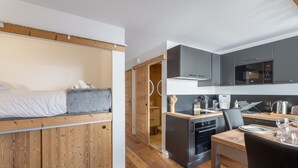 A compact, modern apartment with a kitchenette, a dining area, and a sleeping area with a loft bed.