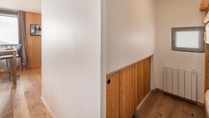 A room with a wooden floor, white walls, a wooden panel accent, a radiator, and a window with blinds.