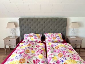 A bedroom with a tufted headboard, floral bedding, two bedside tables with lamps, and a wooden floor. - Vacation home Caroline (Hallschlag)