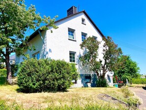 A white building with multiple windows and a chimney, surrounded by trees and bushes. - Vacation home Caroline (Hallschlag)