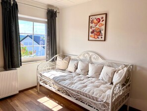A white metal bed with a quilted mattress, a radiator, a window with curtains, and a framed picture on the wall. - Vacation home Caroline (Hallschlag)