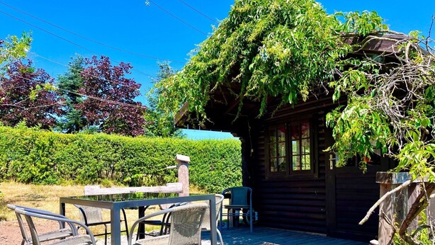 A wooden cabin with a patio area featuring metal chairs and a table.