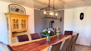 A dining area with a wooden table, wicker chairs, a chandelier, and a cabinet with a sign.