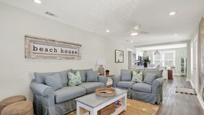 A living room with two grey sofas, a coffee table, and a 'beach house' sign. - Brand New Tybee Beach Home: Walk to Beach (Unit A) (Tybee Island)