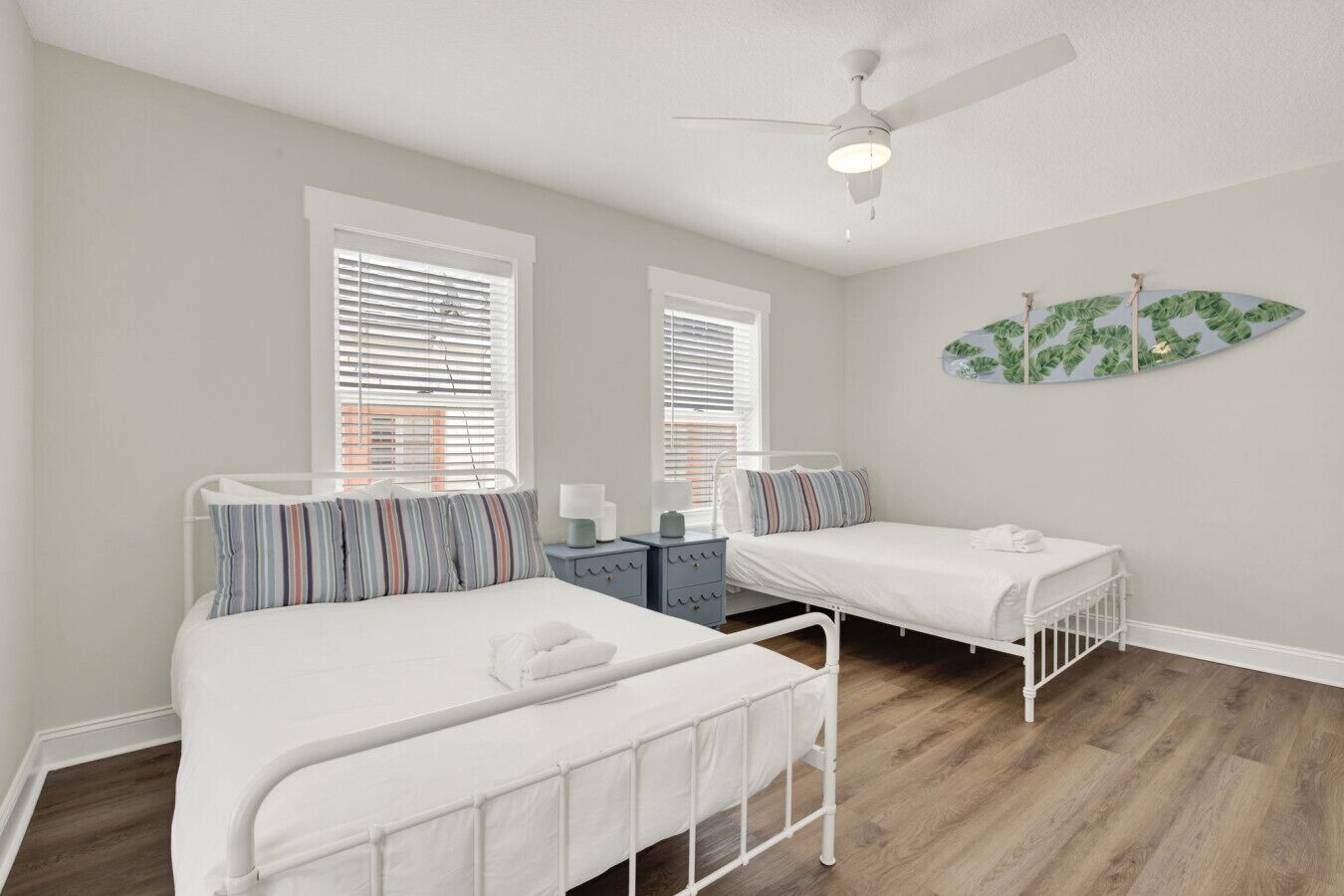 A bedroom with two beds, a ceiling fan, and a wall-mounted plant.