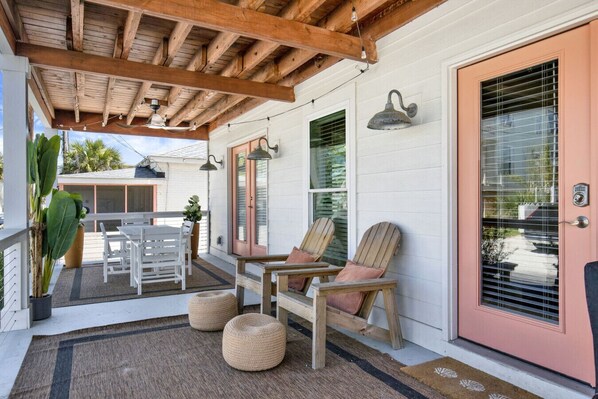 A covered porch with a table and chairs, a door with a window, and a potted plant.