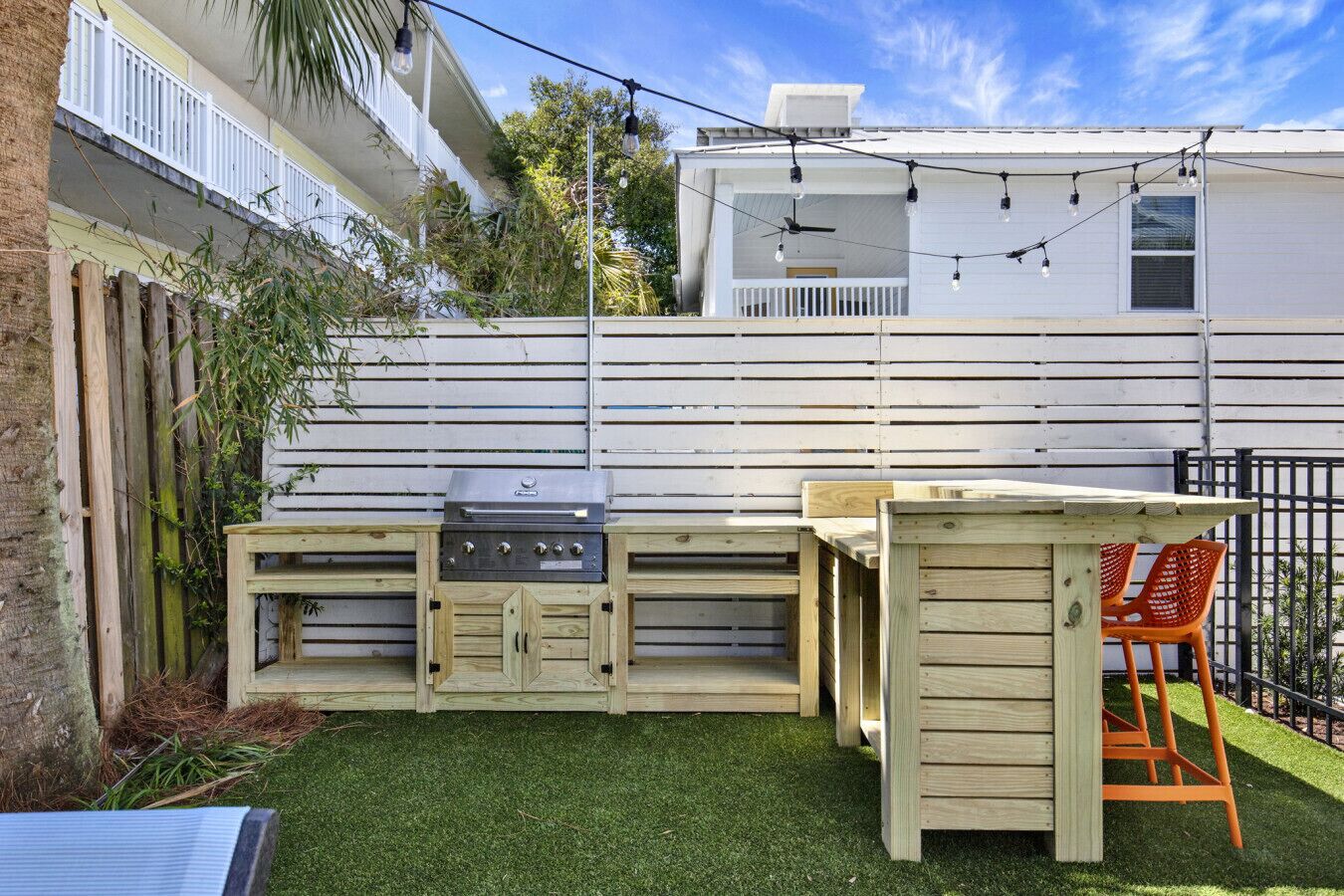 An outdoor kitchen with a grill, wooden cabinets, and a dining area with a chair.