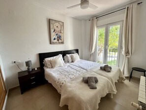 Ein Schlafzimmer mit zwei Betten, einem Nachttisch, einem Deckenventilator und einem Fenster mit Vorhängen.