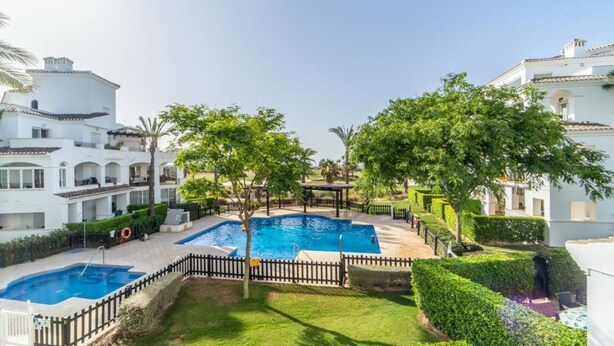 Un quartier résidentiel doté d’une piscine entourée d’une clôture, d’arbres et de bâtiments blancs.