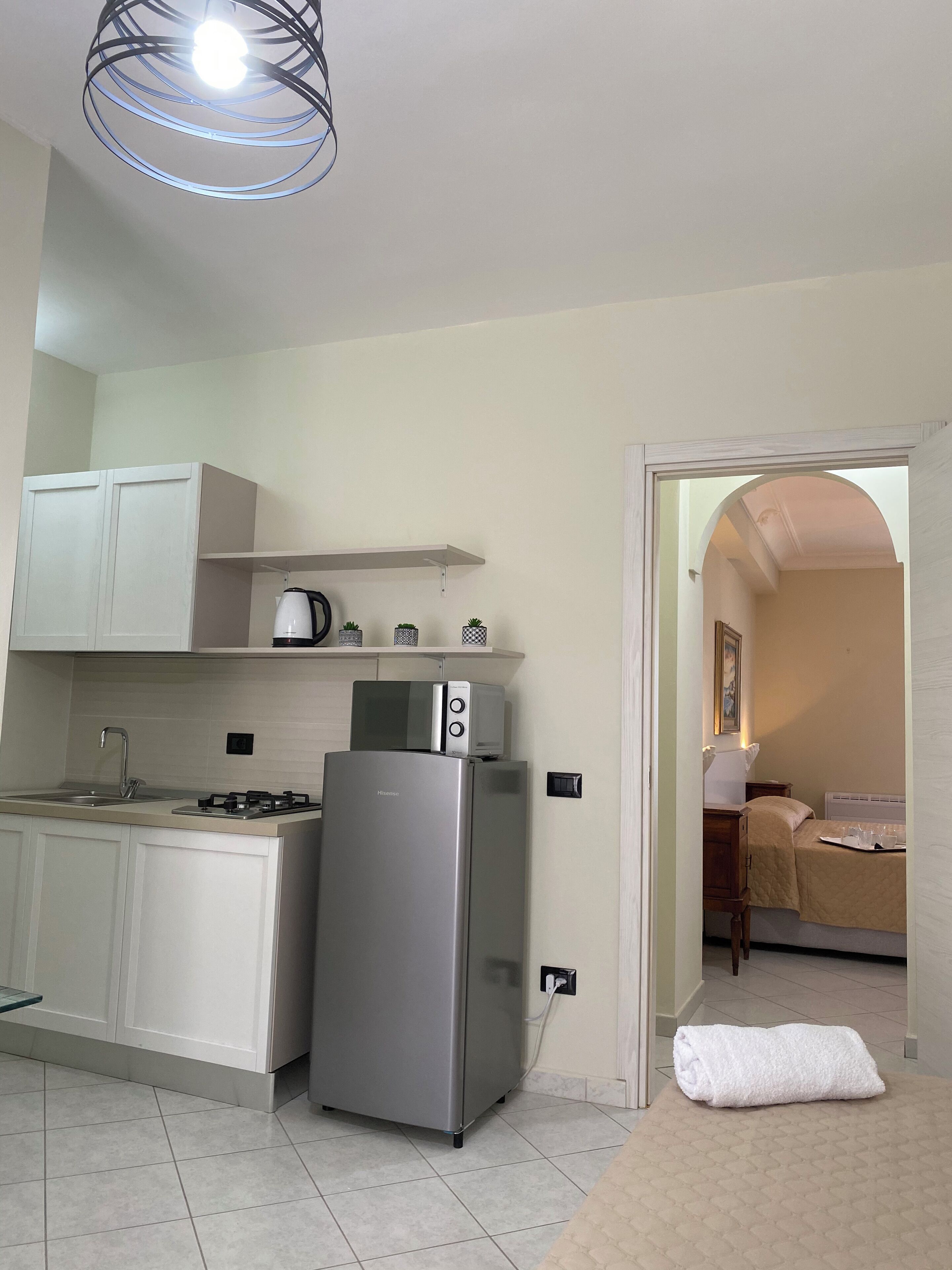 A compact kitchen with a refrigerator, microwave, and gas stove. A white towel is on the floor near the entrance.