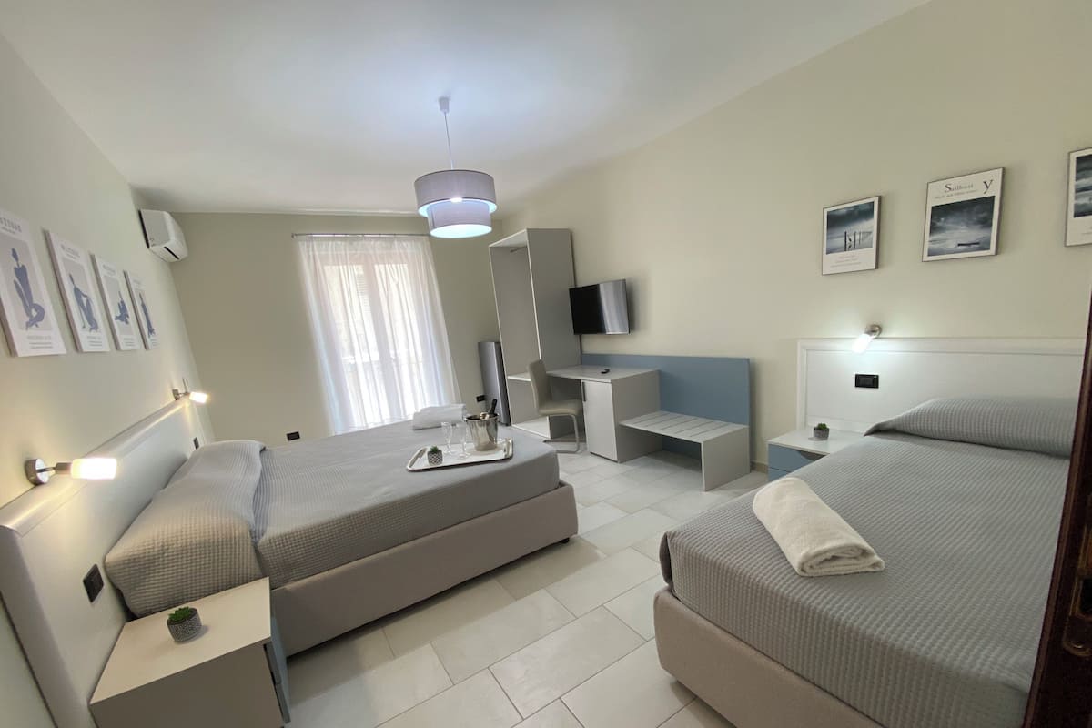 A modern hotel room with two beds, a desk, a TV, and a large window with curtains.