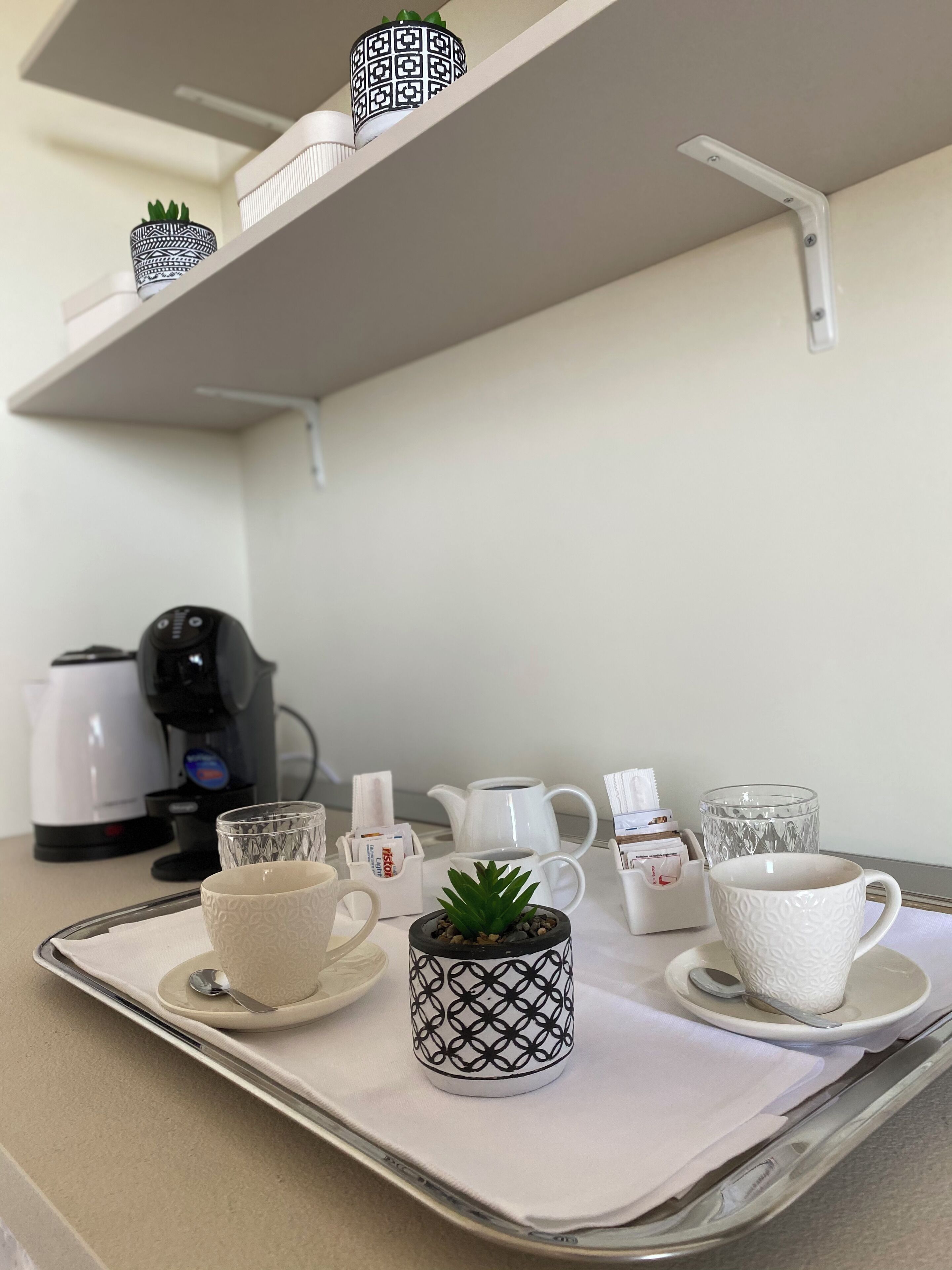 A kitchenette with a coffee maker, a kettle, and various cups and mugs on a tray.
