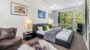Un dormitorio moderno con una cama grande, dos lámparas de noche, un televisor de pantalla plana y vistas a árboles a través de amplios ventanales.