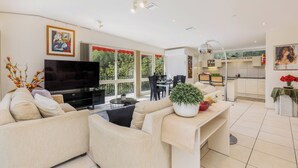 Una sala de estar moderna con un televisor de pantalla plana, sofás color beige, una zona de comedor y una cocina.
