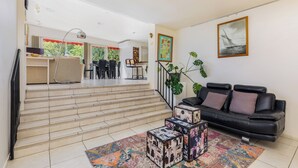 Amplia sala de estar con una escalera que lleva a un comedor, un sofá de cuero negro y un tapete colorido.