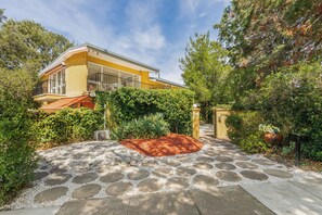 Stunning home surrounded by lush greenery, featuring a balcony and staircase, with a stone pathway leading to the entrance.