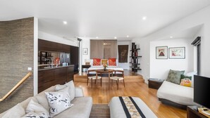 A modern apartment with a kitchen, dining area, and living room. There is a sofa, a TV, and a bookshelf. - Sea Zen - Couples studio with steam shower and spa (Separation Creek)