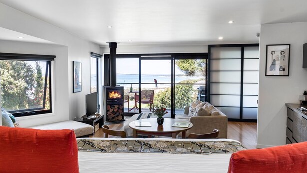 A modern room with a fireplace, a sofa, a dining table, and large windows overlooking a scenic view. - Sea Zen - Couples studio with steam shower and spa (Separation Creek)