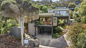 A modern two-story house with a covered patio, a water tank, and a garden with various plants and flowers. - Sea Zen - Couples studio with steam shower and spa (Separation Creek)