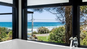 A bathroom with a large window offering a view of the ocean and coastal vegetation. - Sea Zen - Couples studio with steam shower and spa (Separation Creek)