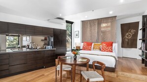 A modern hotel room with a kitchen, a dining area, and a large bed with decorative pillows. - Sea Zen - Couples studio with steam shower and spa (Separation Creek)