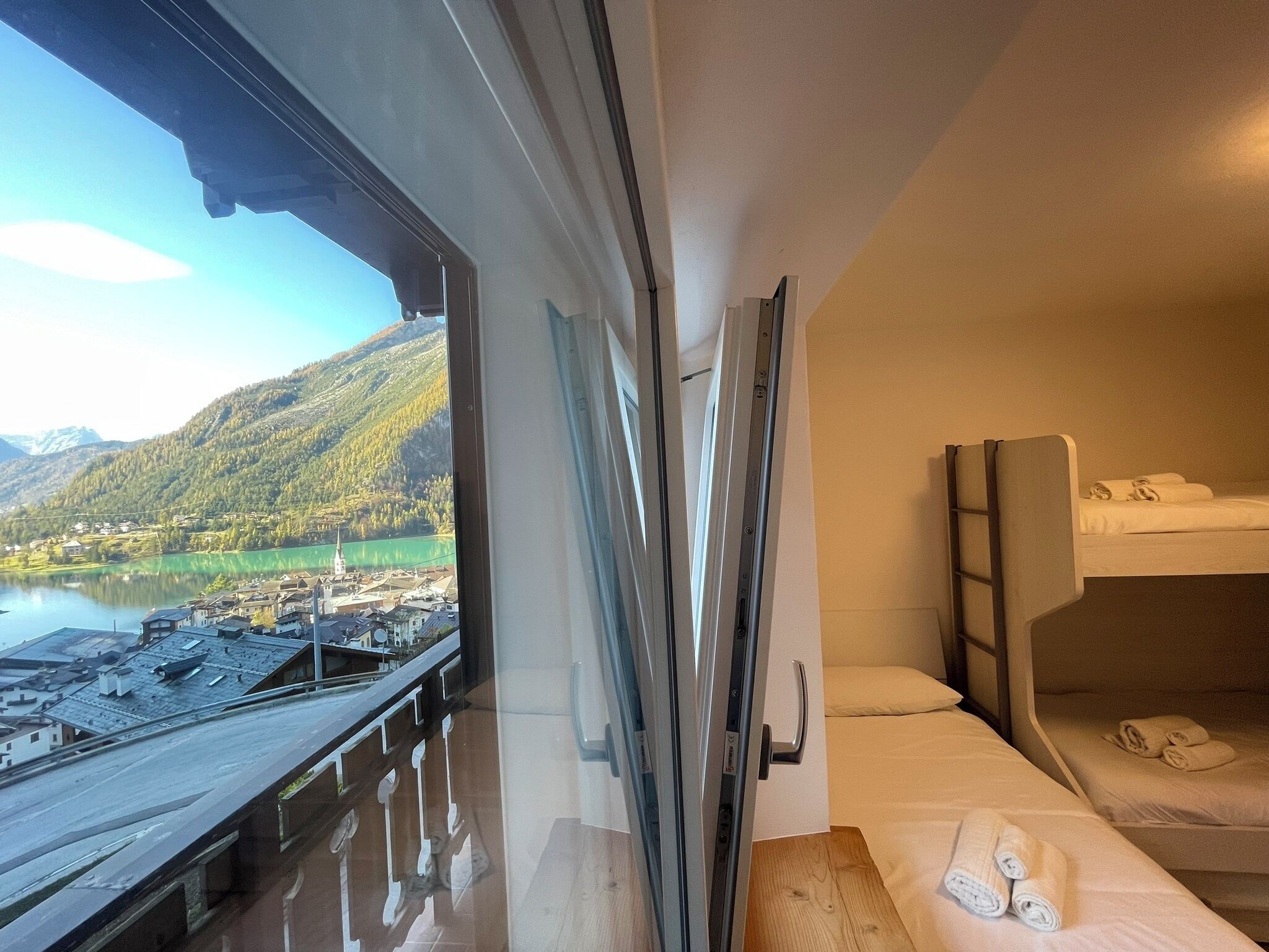Une chambre d’hôtel avec un lit, une table en bois et une fenêtre donnant sur un lac et des montagnes.
