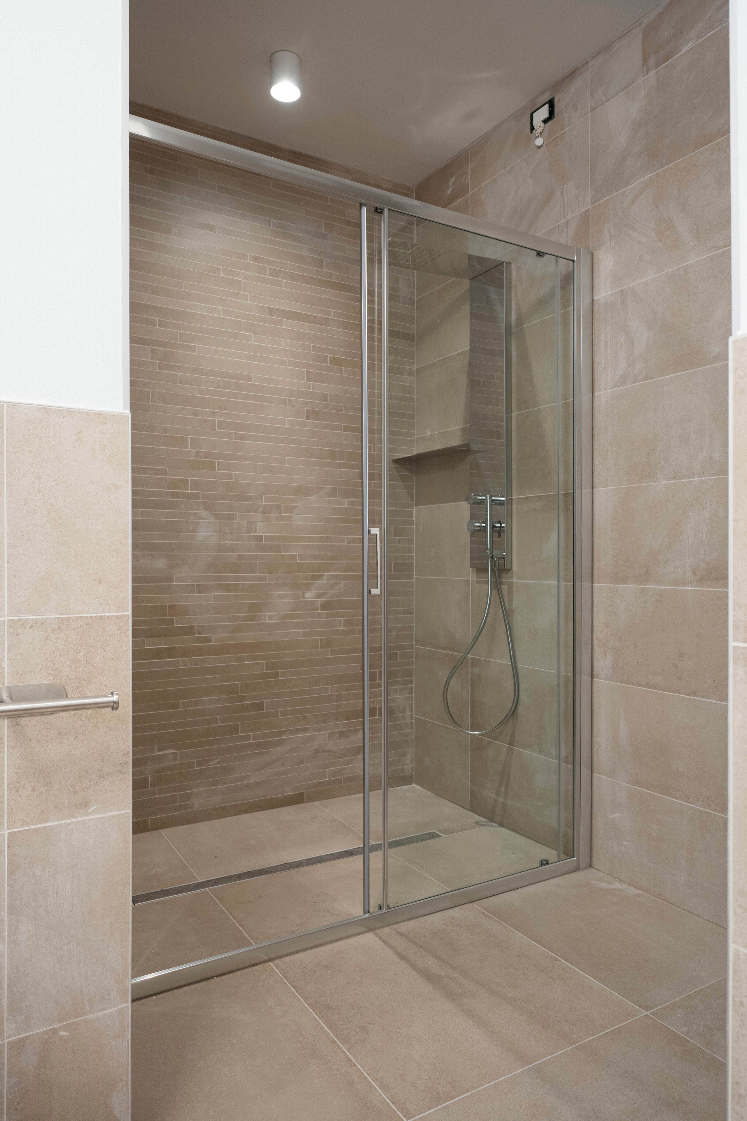 A glass-enclosed shower with a tiled floor and walls, a handheld showerhead, and a control panel.
