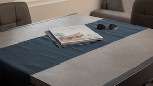 A modern room with a large window, a table with a book and sunglasses, and a sofa. - SnowLake Suite & Apartments (Alleghe)