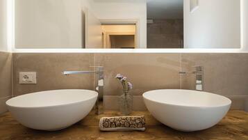 A bathroom with two large white vessel sinks, a wooden countertop, a small vase with flowers, and a mirror above the sinks.