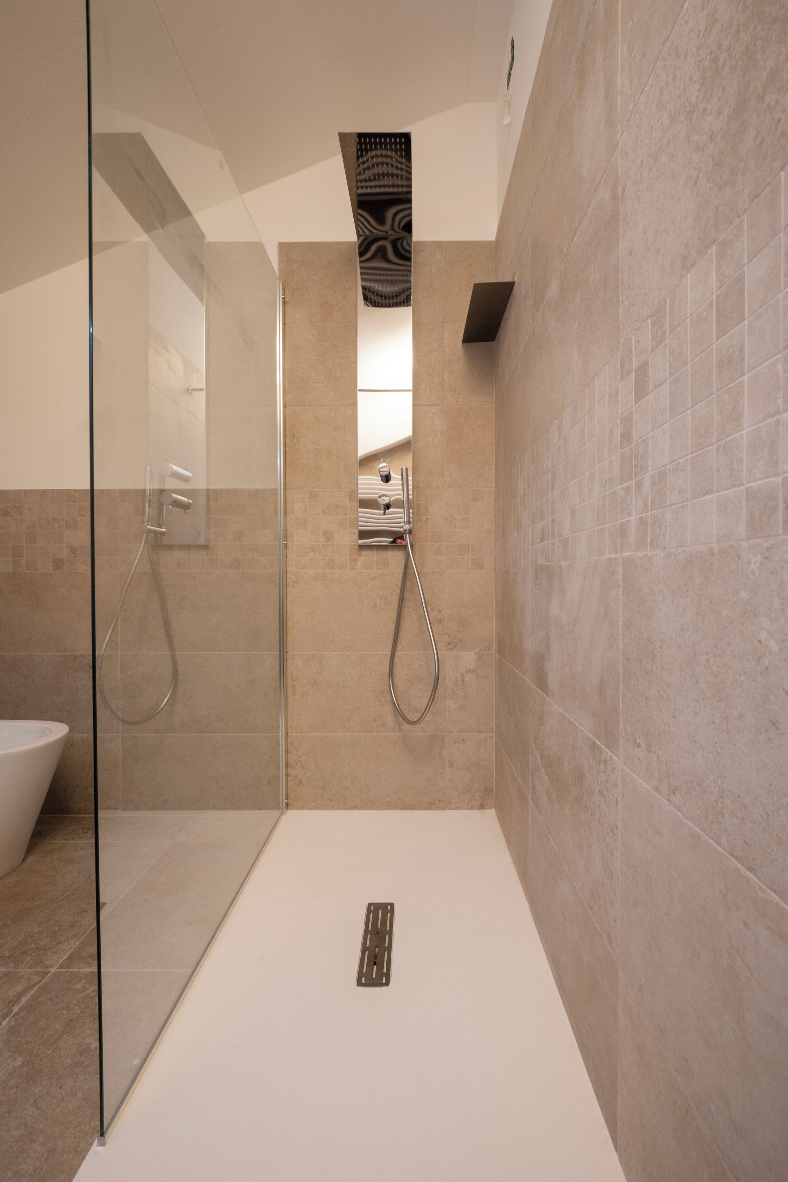 Un baño moderno con cabina de ducha de vidrio, un lavamanos blanco y paredes cubiertas de baldosas beige.