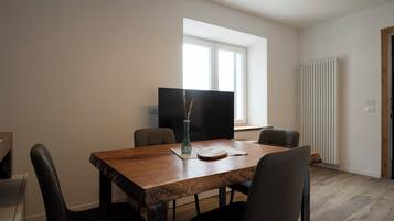 A dining area with a wooden table, four chairs, a vase, and a flat-screen TV.