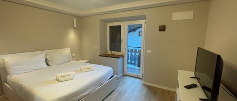 A bedroom with a bed, a TV, and a balcony.